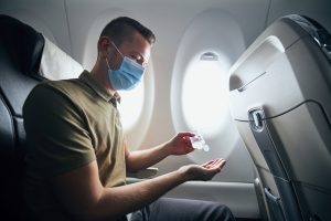 Man in mask sanitizing his hands on airplane