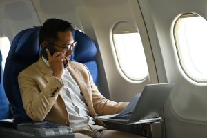 Businessman seated on private airplane, talking on phone while looking at computer screen.