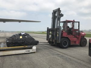 Fork lift placing a loaded air freight pallet onto a K loader next to an airplane