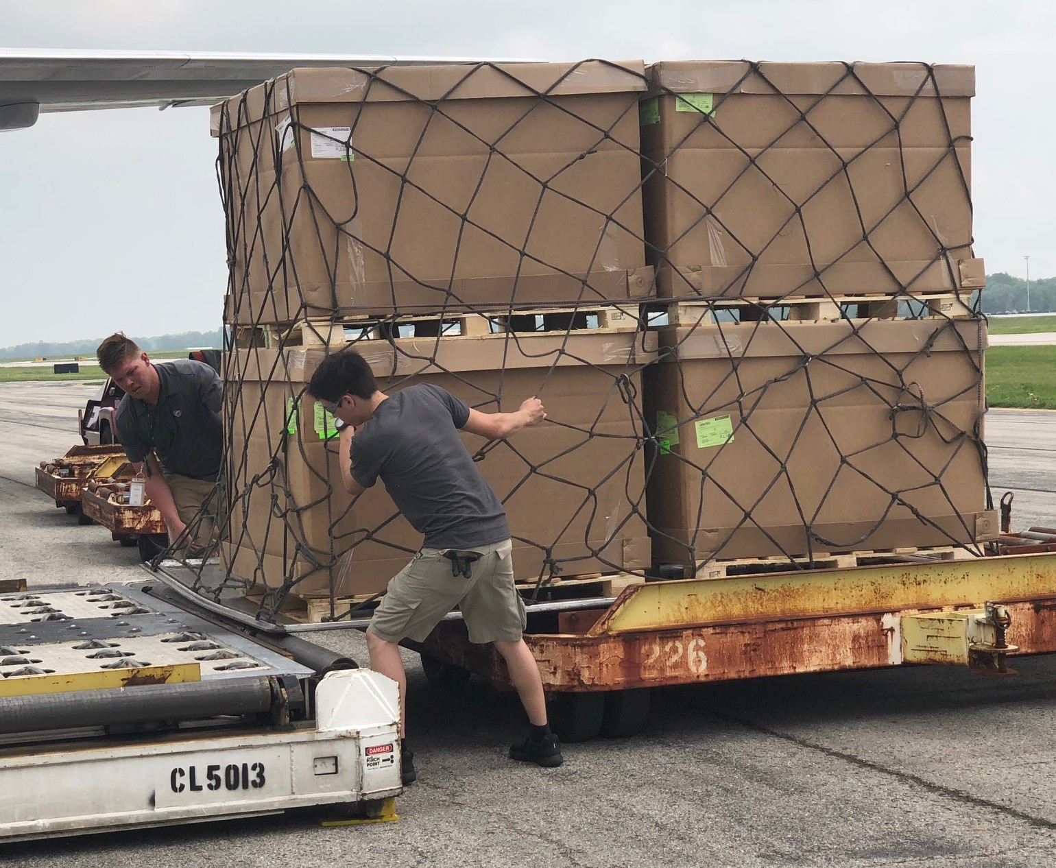 Ground crew workers loading palletized, netted cargo onto airplane platfor